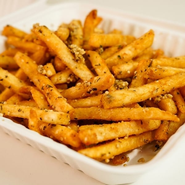 Golden french fries seasoned with herbs and garlic, served in a white takeout container.